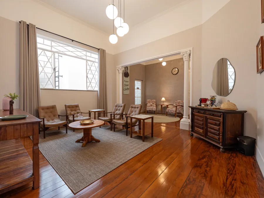 Sala de estar com poltronas de couro, aparador antigo e o arco para o Espaço Dona Gladys