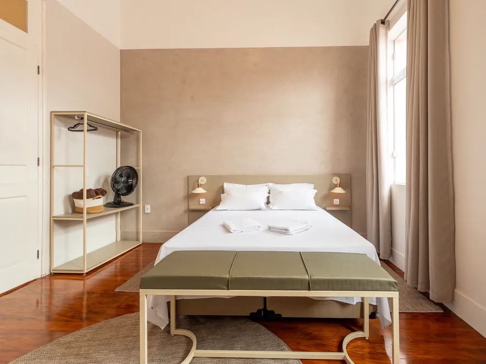 Quarto de casal com banqueta ao pé da cama, arara e parede de cimento queimado