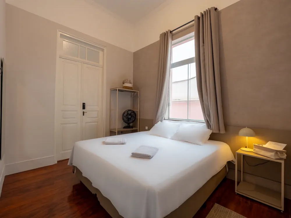 Quarto de casal com janela, abajur de cabeceira e roupeiro