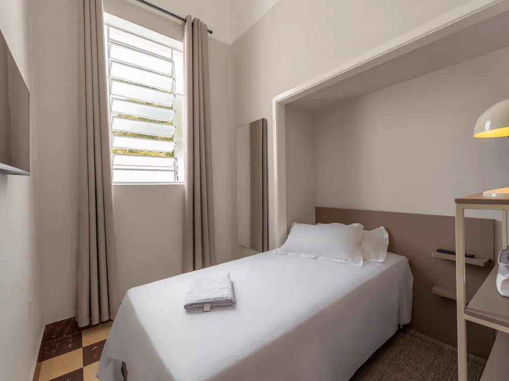 Quarto de solteiro com televisão, janela basculante e piso xadrez